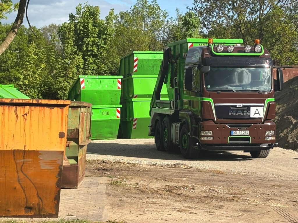 Abfallcontainer LKW steht vor grünen Container auf einem Hof bei sonnigen Wetter